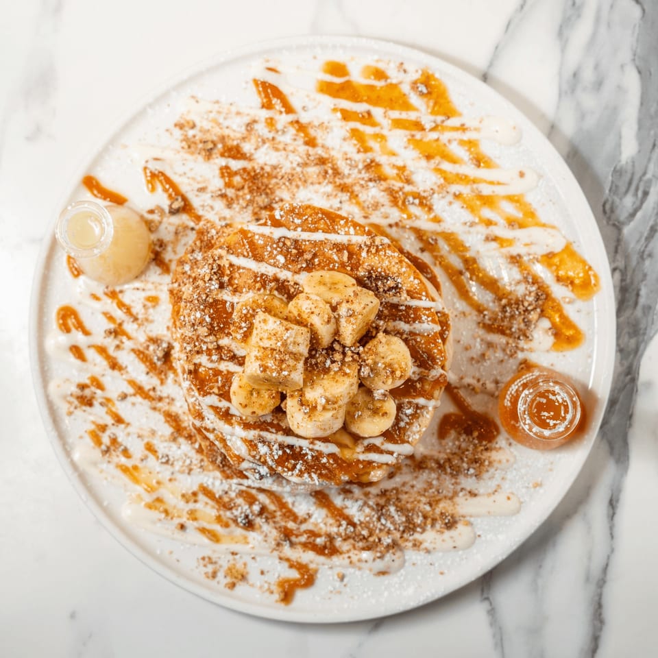Golden waffles topped with sliced bananas, powdered sugar, nuts, caramel, and cream drizzle.