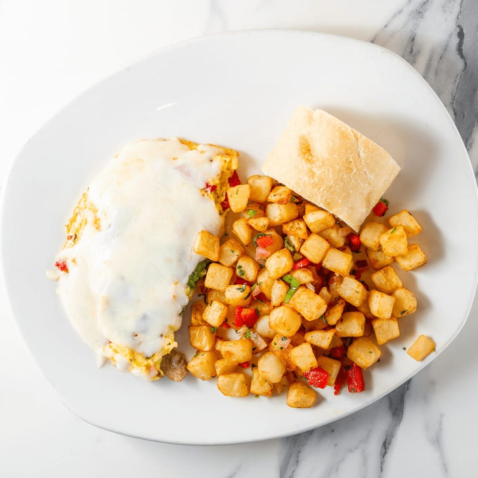 Omelet covered in melted cheese, served with seasoned breakfast potatoes and a piece of toast.