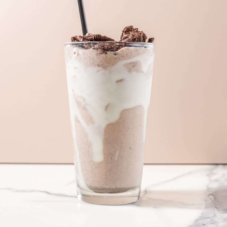 A tall glass of cookies and cream milkshake with a black straw on a marble surface.
